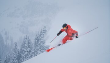 © INTERSPORT International Corporation GmbH Skifahrer in roter Kleidung fährt einen verschneiten Hang hinunter. | © INTERSPORT International Corporation GmbH