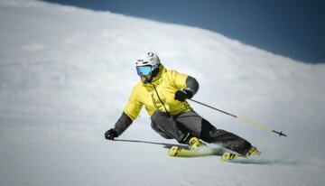 Skifahrer in gelber Jacke fährt eine schneebedeckte Piste hinunter. | © Fischer Sports GmbH