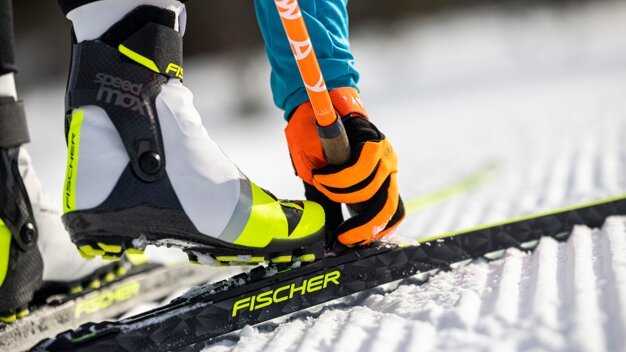 Langlaufschuh auf Ski mit orangefarbenen Handschuhen. | © Fischer Sports GmbH