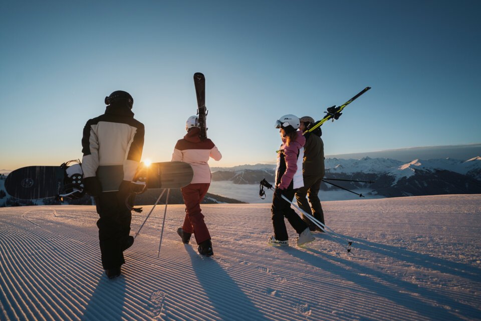 Gruppe von Skifahrern und Snowboardern beim Sonnenuntergang auf einer präparierten Piste. | © INTERSPORT International Corporation GmbH