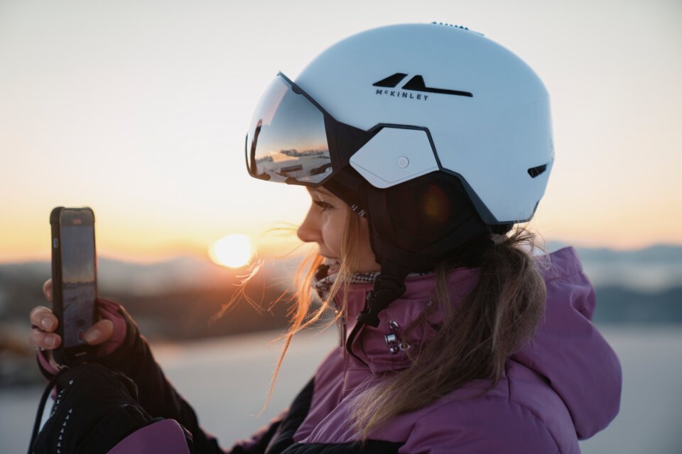 © INTERSPORT International Corporation GmbH Frau mit Skihelm filmt Sonnenaufgang mit Handy | © INTERSPORT International Corporation GmbH