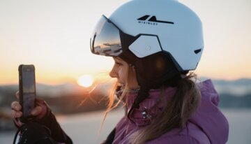 © INTERSPORT International Corporation GmbH Frau mit Skihelm filmt Sonnenaufgang mit Handy | © INTERSPORT International Corporation GmbH