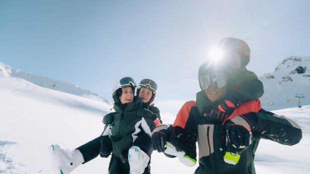 Vater trägt zwei Kinder auf seinen Schultern im Schnee.