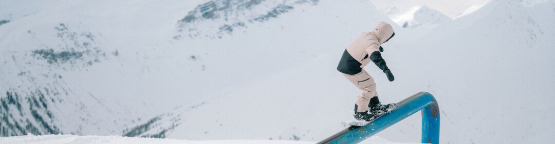 Snowboarder fährt auf einer blauen Rail vor Bergkulisse.