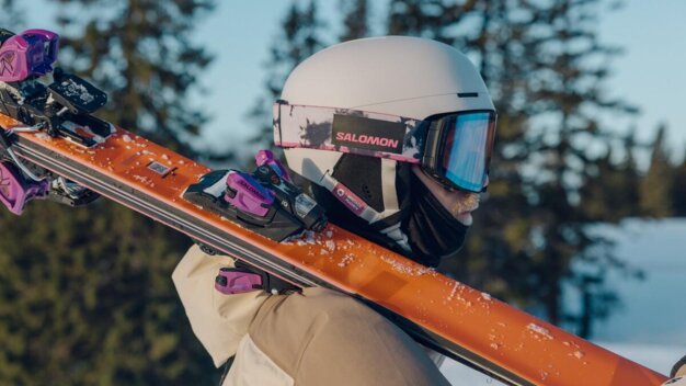 Person mit Skihelm und Skiern über der Schulter.