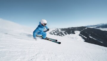 Skifahrerin in blauer Jacke fährt einen verschneiten Hang hinunter. | © INTERSPORT International Corporation GmbH