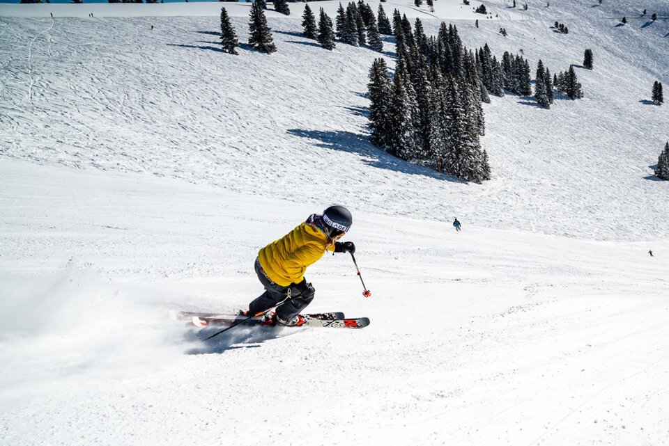 Skifahrer in gelber Jacke fährt auf schneebedeckter Piste