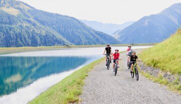 Eine Familie fährt mit Fahrrädern entlang eines Sees in den Bergen.