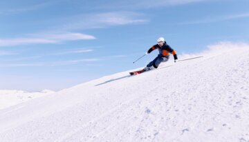 Skifahrer auf einer schneebedeckten Piste unter blauem Himmel.